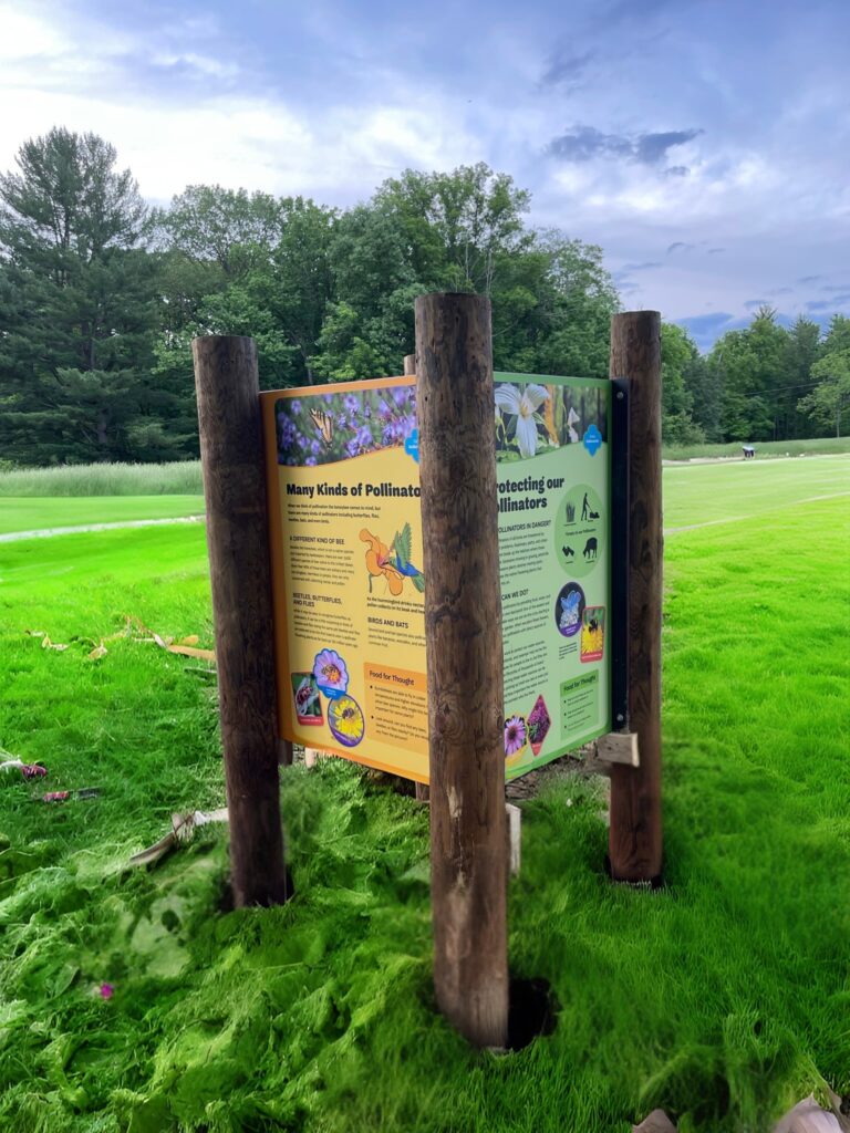 Natural logs support the four corners of this outdoor exhibit sign that teaches about pollinators