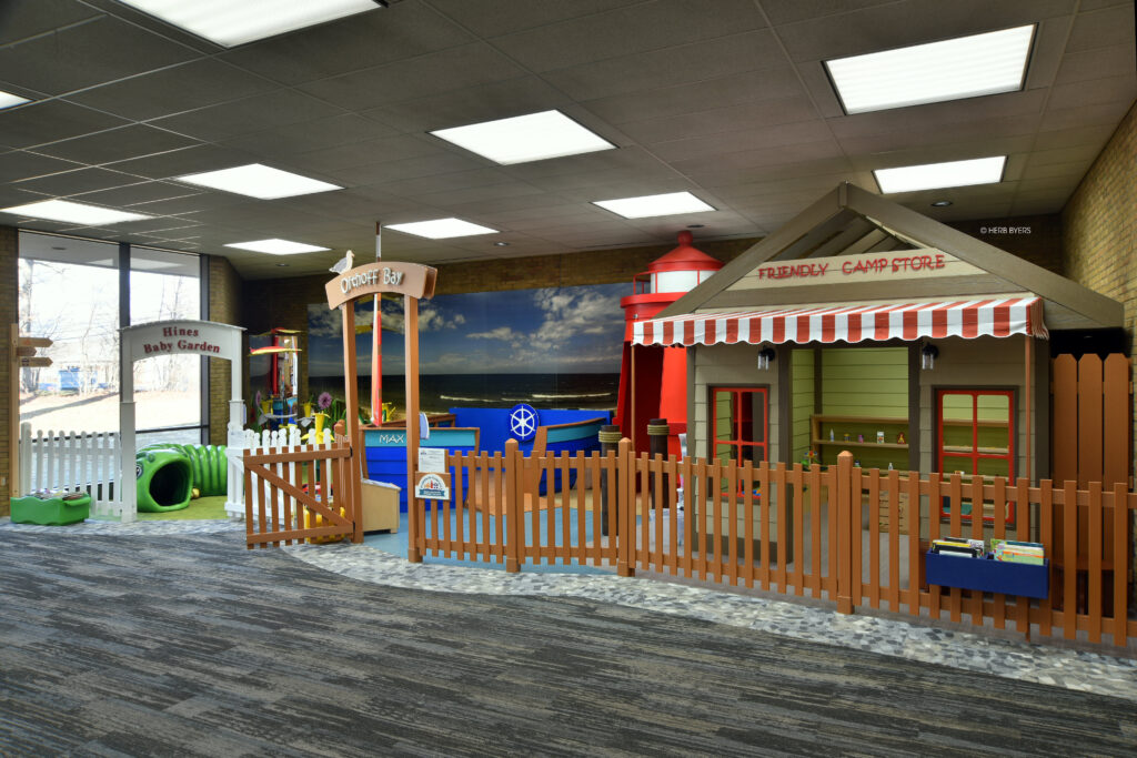 Custom-designed and fabricated themed play space featuring a friendly campstore, a lighthouse, and baby garden area.