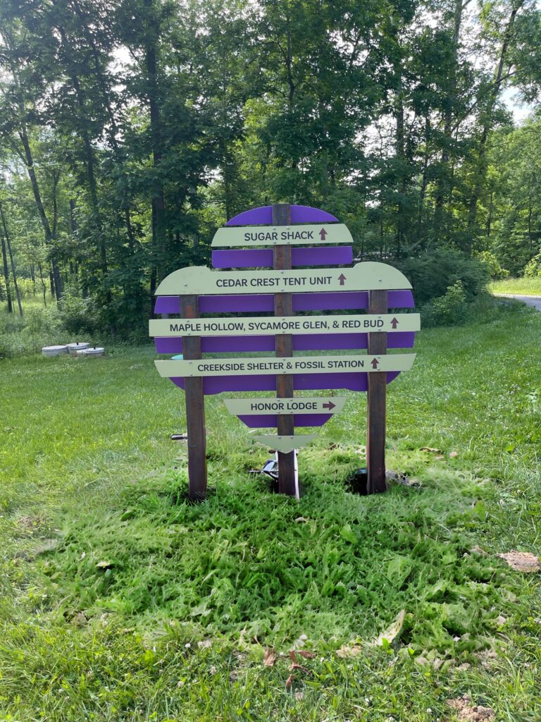 In the shape of the Girl Scouts logo, this directional outdoor signage shows how to get to various places at Stonybrook camp