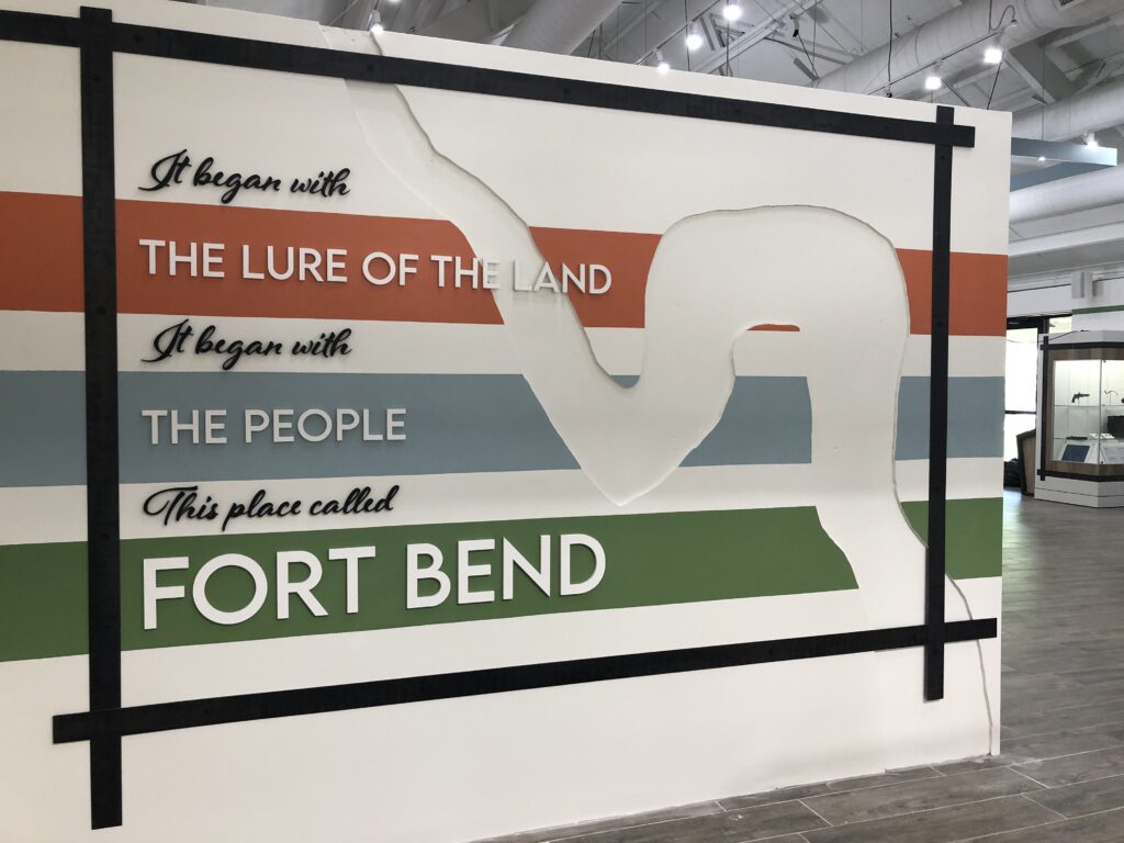 Custom-designed entryway sign to the museum exhibits. Sign says, it began with the lure of the land, it began with the people, this place called Fort Bend